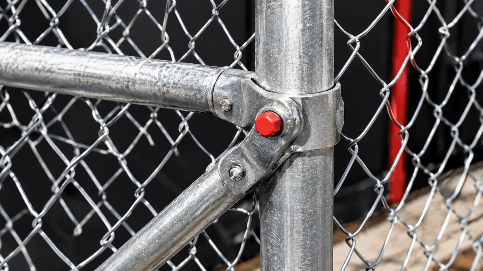 Galvanised brace fitting connecting a diagonal rail to a chain link fence post.
